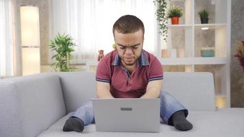 giovane uomo con nanismo Lavorando in linea su il computer portatile a partire dal casa gioia e ridendo. uomo con nanismo Lavorando in linea su il computer portatile a partire dal casa dire bugie su divano e sorridente e gioia mentre utilizzando il computer portatile. video