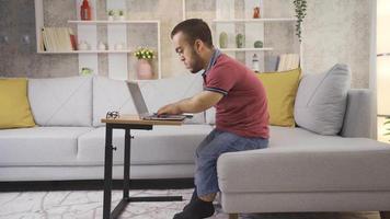 jovem masculino aluna com nanismo estudando às casa usando computador portátil. Faculdade aluna jovem homem com nanismo estudando às lar, Desativado jovem aluna usando computador portátil. video