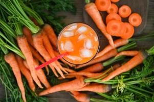 jugo de zanahoria en el fondo de la mesa de madera, zanahorias frescas y dulces para cocinar frutas y verduras para el concepto de salud, jugo de zanahorias frescas en vidrio con hielo en verano foto