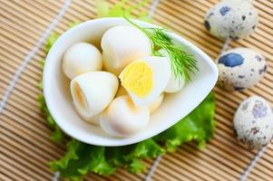 boiled eggs food, quail eggs on white bowl, breakfast eggs with fresh quail eggs and vegetable lettuce on table background - top view photo