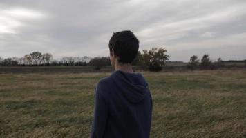 joven hombre, Adolescente chico vistiendo azul camisa de entrenamiento soportes en campo a puesta de sol video