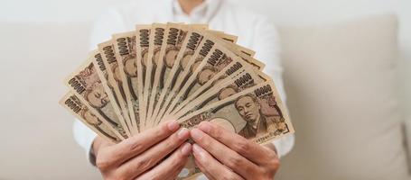 man hand holding Japanese Yen banknote stack. Thousand Yen money. Japan cash, Tax, Recession Economy, Inflation, Investment, finance and shopping payment concepts photo