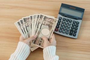 Woman hand counting Japanese Yen banknote with calculator. Thousand Yen money. Japan cash, Tax, Recession Economy, Inflation, Investment, finance, savings, salary and payment concepts photo