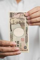 mano de hombre sosteniendo la pila de billetes de yen japonés. dinero de mil yenes. conceptos de pago en efectivo, impuestos, economía de recesión, inflación, inversión, finanzas y compras de japón foto