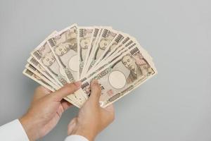 mano de hombre sosteniendo la pila de billetes de yen japonés. dinero de mil yenes. conceptos de pago en efectivo, impuestos, economía de recesión, inflación, inversión, finanzas y compras de japón foto