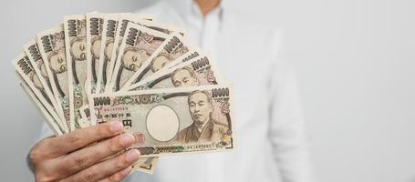 mano de hombre sosteniendo la pila de billetes de yen japonés. dinero de mil yenes. conceptos de pago en efectivo, impuestos, economía de recesión, inflación, inversión, finanzas y compras de japón foto