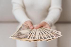 mano de mujer sosteniendo la pila de billetes de yen japonés. dinero de mil yenes. conceptos de pago en efectivo, impuestos, economía de recesión, inflación, inversión, finanzas y compras de japón foto