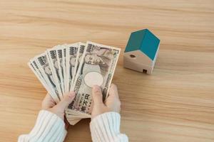 mujer con billete de yen japonés y modelo de casa. conceptos inmobiliarios, domésticos, hipotecarios, efectivo de Japón, impuestos, economía de recesión, inflación, inversión, finanzas y ahorro foto