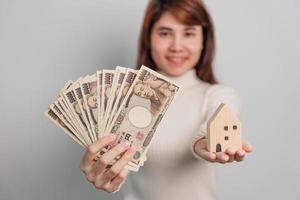 mujer con billete de yen japonés y modelo de casa. conceptos inmobiliarios, domésticos, hipotecarios, efectivo de Japón, impuestos, economía de recesión, inflación, inversión, finanzas y ahorro foto