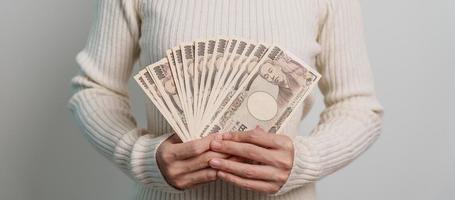 mano de mujer sosteniendo la pila de billetes de yen japonés. dinero de mil yenes. conceptos de pago en efectivo, impuestos, economía de recesión, inflación, inversión, finanzas y compras de japón foto