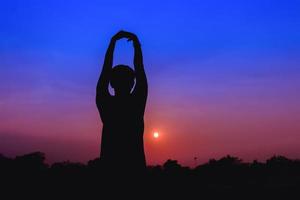 silueta de masculino meditando y yoga practicando con ejercicio a amanecer en público parque Mañana foto