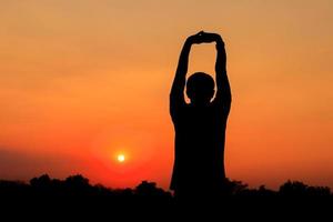 Silhouette of male meditating and yoga practicing with exercise at sunrise in public park morning photo