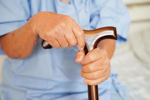 Asian elderly disability woman patient holding walking stick in wrinkled hand at hospital. photo