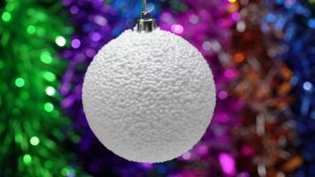 spinning vit xmas boll på suddigt bokeh bakgrund av färgad och lysande glitter, Semester lampor. närbild se av hängande enda Semester jul boll. rörelse fläck. selektiv fokus på förgrund