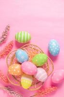 Happy Easter holiday greeting card concept. Colorful Easter Eggs and spring flowers on pastel pink background. Flat lay, top view, copy space. photo