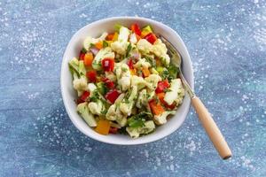 Ensalada de coliflor saludable en tazón blanco sobre fondo de madera azul. foto