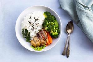 sano comida A la parrilla pollo tiene arroz brócoli Zanahoria vegetales en plato en azul madera mesa.