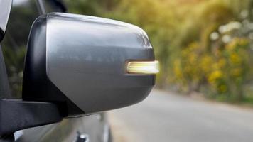 Mirror wing of gray with turn light signal. Blurred of asphalt road and trees with yellow flower for background. photo