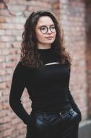 Beautiful young woman with brunette curly hair, portrait in eye glasses enjoying the sun in the city. photo