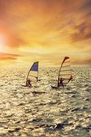 two man playing wind surf over rushing sea against beautiful sunset lighting photo