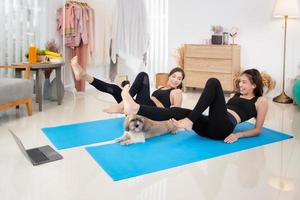 Two beautiful Asian girls wearing workout clothes and smiling with dogs in bedroom. woman on exercise mat with dumbbells and tablet photo