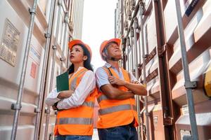 asian woman Engineer with note clipboard and asian man Supervisor in Hard Hats and Safety Vests Stand in Container Terminal. Container in export and import business and logistics. photo