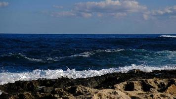 Blue sea wave and white foam and splash. Stone beach on island of Malta, no sandy beach. Summer holiday border frame concept. Tropical island vacation backdrop. Tourist travel banner design template. photo