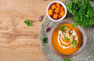 Pumpkin soup in a bowl served with parsley and croutons. Vegan soup. Thanksgiving day food. Halloween meal. Top view photo