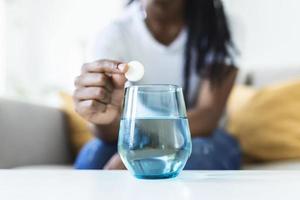 de cerca de un joven mujer goteante un efervescente neutralizador de acidez en un vaso de agua. joven mujer difícilmente poner un soluble píldora con un medicina para dolor o un resaca en un vaso de agua foto