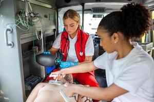 paramédico utilizando desfibrilador aed en conductible un básico cardiopulmonar resucitación. emergencia cuidado asistente poniendo silicona manual resucitadores en un ambulancia. foto