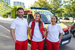 Tres paramédicos por el ambulancia. joven mujer y hombre sonriente. médico es que lleva un médico trauma bolsa. foto