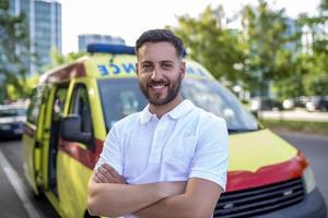 joven hombre , un paramédico, en pie a el posterior de un ambulancia, por el abierto puertas él es mirando a el cámara con un confidente expresión, sonriente foto