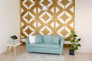 Living room in the Scandinavian style. Geometric carved panel on the wall, blue sofa, indoor plant ficus, coffee table in the house photo