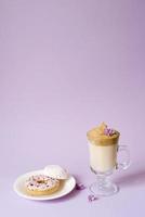 Beautiful dalgona drink a frothy coffee in a transparent mug and flowers of lilac on a purple background. Sweets on a plate photo