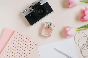 Vintage retro camera and pink tulip flowers with blank notebook on beige background. Feminine blogger flat lay. top view. Spring concept mock up. photo