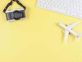 flat lay of airplane model, computer keyboard, and digital camera with copy space on yellow background, business and traveling concept. photo