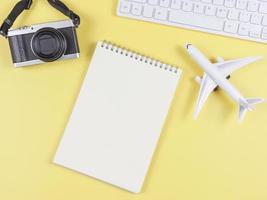 flat lay of airplane model, computer keyboard, opened blank page notebook and digital camera with copy space on yellow background, business and traveling concept. photo