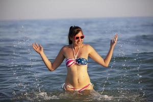 Happy middle aged woman splashing sea water in swimsuit with American flag print. photo