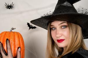 Young woman in black hat and costume on white background decorated with spiderweb and bats holding pumpkin.Halloween and autumn concept. photo