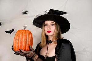 Evil witch in the black with red lips holdin pimpkin. Halloween costume party photo
