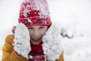 contento pequeño chico en invierno en cubierto de nieve mitones. foto