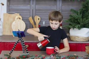 A portrait of a confident and creative child blogger talking to the camera at home in the kitchen, he is vlogging. A little boy is recording a stream on a smartphone. photo