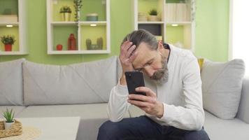 Middle aged man using smartphone in thoughtful and anxious state. Middle-aged man at home focused on smartphone looking thoughtfully and nervously. video