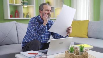 Middle aged freelancer man working in living room at home using laptop. Middle aged man sitting on sofa at home working looking at projects and documents, working online using laptop. video