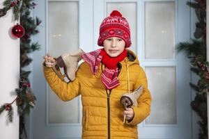 Handsome little boy in bright clothes holds old skates against the background of Christmas decorations. photo