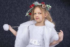 Beautiful little girl in a white fur coat with a Christmas wreath on a gray background. Christmas child. photo