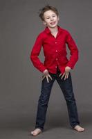 Handsome boy in a red shirt and jeans on a gray background. A child in the modeling business is posing. photo