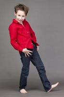 Handsome boy in a red shirt and jeans on a gray background. A child in the modeling business is posing. photo