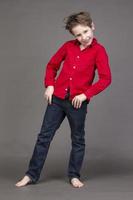 Handsome boy in a red shirt and jeans on a gray background. A child in the modeling business is posing. photo