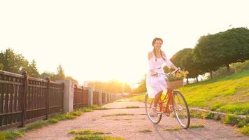 jovem lindo mulher sentado em dela bicicleta com flores às pôr do sol video